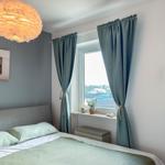 Schlafzimmer mit Bett, Fenster, Vorhängen und Deckenleuchte.