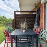 Terrasse mit Tisch und Stühlen, Sicht auf Grünflächen und Holzgeländer.