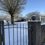 Schneebedeckter Garten mit Zaun und Terrasse im Hintergrund.