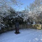 Schnee bedeckt einen Garten mit Steinmauer und einer dunklen Skulptur.