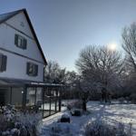 Schneebedecktes Haus mit Wintergarten und schneebedeckten Bäumen im Garten.