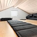 Attic room with mattresses and pillows on wooden floor under wooden ceiling