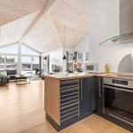 Kitchen with stainless steel appliances and wood surfaces. Living area with sofa and large windows.