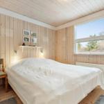 A bedroom with wooden walls, bed, two chairs, and window. 