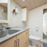 Bathroom with sink, toilet, and shower. Wooden ceiling and light walls.