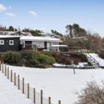 Black house with terrace and snow-covered garden. Wooden railings and steps lead to the entrance.