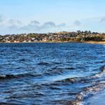 Beach with waves, view of inhabited hills in the background.
