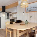 Dining area with wooden table and chairs. Kitchen in background. Wooden walls and ceiling.