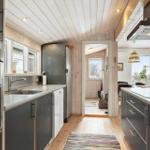 Kitchen with gray cabinets, stainless steel sink, and wooden floor. Corridor to living area.