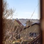 View from a window shows a house with a red roof and a lake in the background.