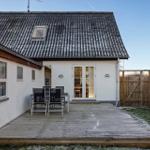 House with wooden terrace, garden, and garden gate. Outdoor table with chairs. Roof with skylight.