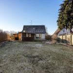 House with garden, terrace, and wooden garage. Lawn with frost. Tall tree on the right.