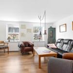 Living room with wooden floor, sofa, chairs, and table. Pictures hang on the walls.