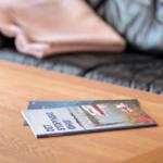 A book rests on a wooden table in front of a sofa with a blanket.