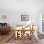 Dining room with wooden table, chairs, and rug. Living area with sofa and armchair. Window to outdoor terrace.