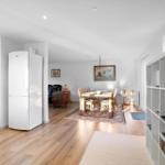 Kitchen with fridge and oven. Dining area with table and chairs. Living area with leather sofa.