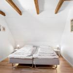 Two beds in an attic room with wooden beams and wall pictures.
