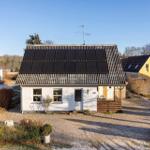 A white house with solar panels on the roof, garden, and neighboring houses.