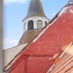From the window, a church tower with clock and pointed roof is visible, surrounded by red roofs.