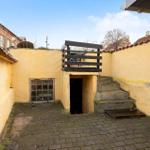 Backyard with yellow walls, stone paving, and wooden terrace above entrance.