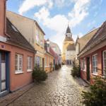 A cobblestone street with colorful houses and a tower in the background.