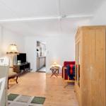 Living room with wooden floor, wardrobe, and view into the kitchen.