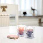 Two lit candles in glasses and a deck of cards are on the table.