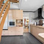 Kitchen with wooden cabinets, range hood, and kitchen island. Staircase on the left.