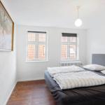Bedroom with bed, two windows, and wooden floor. Two pictures hang on the wall.