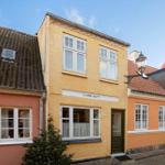 Yellow house with green door and white windows on a street with other houses.