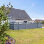 Haus mit grauem Dach und Zaun auf grünem Grundstück unter blauem Himmel.