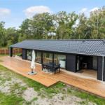 Modern cabin with wooden terrace, garden table, and view of forest.
