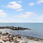 Beach with rocks and calm sea under blue sky with white clouds.