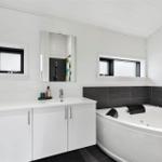 Bathroom with bathtub, sink, and mirror. White walls and black tiles.