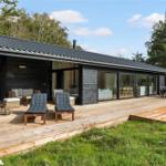 Modern wooden cabin with large wooden terrace, lounge area, and view into the forest.