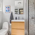 Bathroom with shower, sink, and toilet. Terrazzo tiles and wooden cabinet.