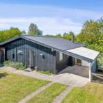 Black wooden house with patio and garden. Surrounded by trees and greenery.
