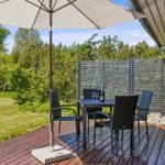 Deck with table, four chairs, and umbrella. Background: green lawn and wooden railing.