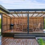 Wooden terrace with seating, grill, and pergola under a roof.