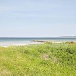Green grass leads to a beach with a view of the sea and distant horizon.