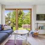 Living room with sofa, table, and TV. Green view through windows.