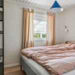 Bedroom with bed, window, and wall lamp. Visible wooden floor and metal shelf.