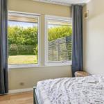 Bedroom with view of green garden and wooden terrace. Bed, curtains, and wooden floor.
