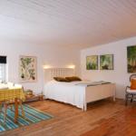 Bedroom with bed, chair, and dining table. Wooden floor and white walls.