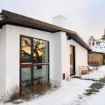 A white house with large windows and a snow-covered garden. A terrace with a table and chairs.