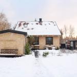 Winter cottage with snow-covered roof, wooden bench, and garden furniture.