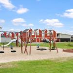 Play area with swings, sandbox, and slide in front of red holiday homes.
