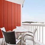 Balcony with table and chairs covered in snow, red wall and white railing.