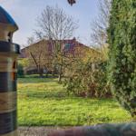 Vorgarten mit Grasfläche, Bäumen und einem Gartenhaus im Hintergrund.