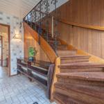 Haus mit Holztreppe, kunstvoller Metallgeländer und Fliesenwand im Eingangsbereich.